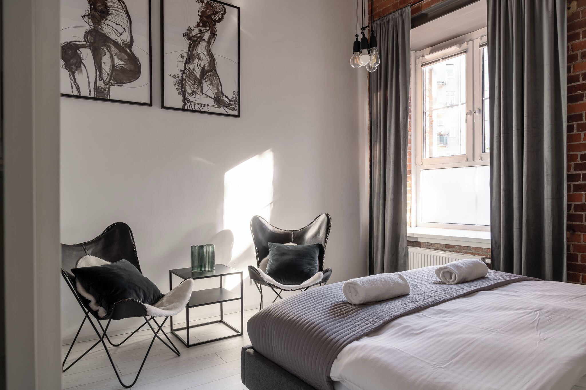 Una camera d'hotel moderna con un letto grande, due poltrone, un tavolino e opere d'arte alle pareti.