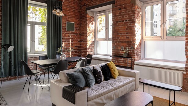 Un salon moderne avec un mur en briques, un canapé blanc, une table à manger et de grandes fenêtres.