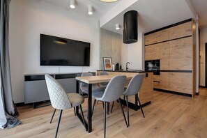 A modern kitchen with a flat-screen TV, wooden cabinets, and a dining area with a table and chairs.