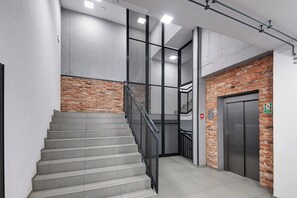 A staircase with metal railings, a brick wall, and an elevator. - RentPlanet - Nowa Papiernia (Wroclaw)