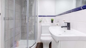 Un baño moderno con cabina de ducha de vidrio, un lavabo blanco y un inodoro.