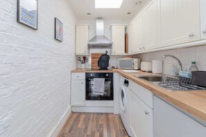 A compact kitchen with white cabinets, a built-in oven, a microwave, a sink, and a dish rack. - Central & Charmingly Curated 1BD Wifi Fulham (London)
