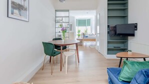 Una sala de estar moderna con comedor, un televisor montado en una pared verde y vistas a la cocina.
