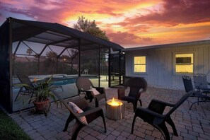 Un patio couvert, aménagé avec du mobilier d’extérieur et un foyer, donnant sur une piscine.