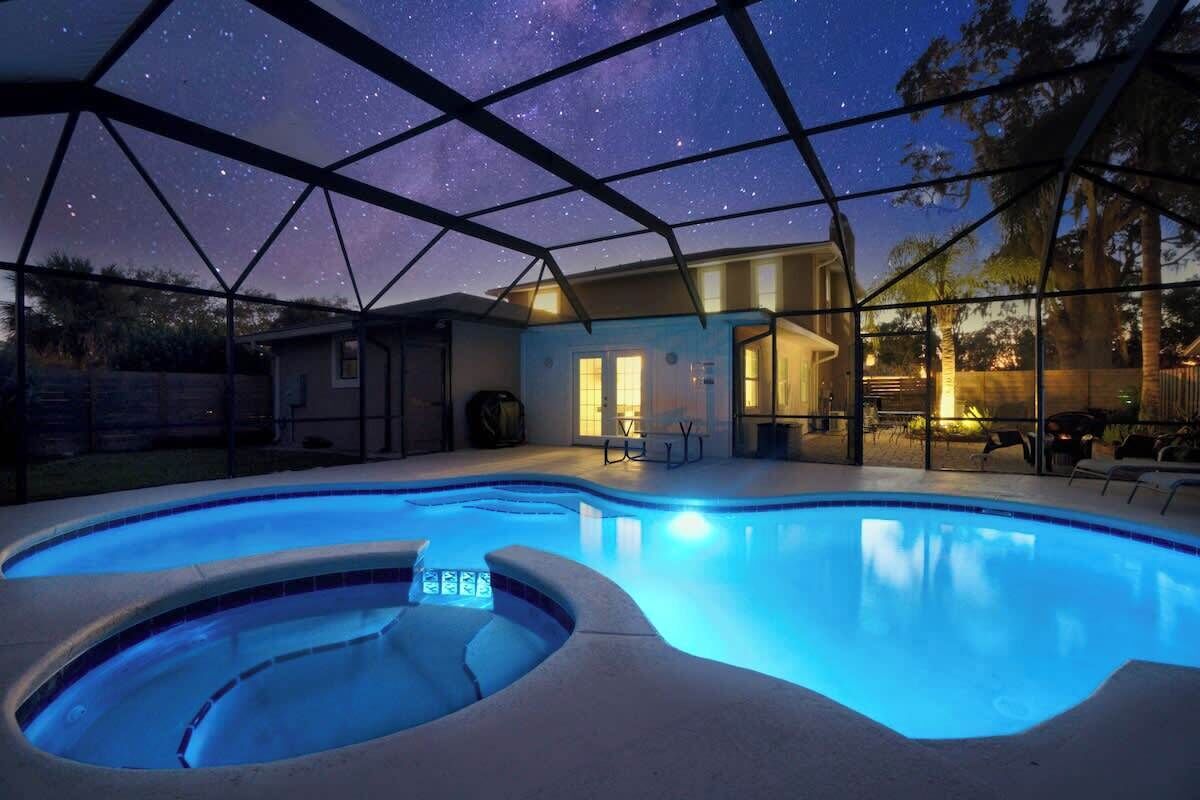 Una piscina con vista a un cielo estrellado, un porche cubierto y una casa con puerta y ventanas visibles.