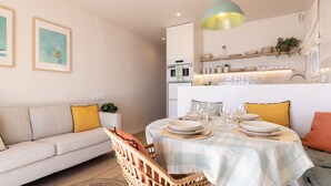 Uma sala de estar moderna com área de jantar, apresentando um sofá, uma mesa de jantar posta com pratos e copos, e um lustre.