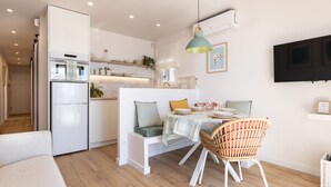 Uma cozinha moderna com geladeira embutida, área de refeições com banco e cadeiras de vime, e uma televisão de tela plana fixada na parede.