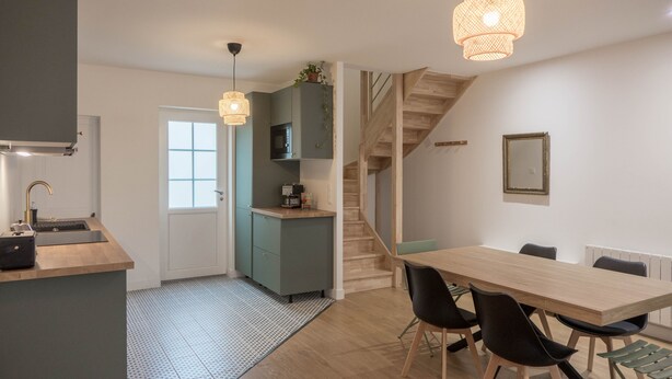 Una cocina moderna con pileta, microondas y placares, un comedor con mesa y sillas, y una escalera que sube a otro nivel.