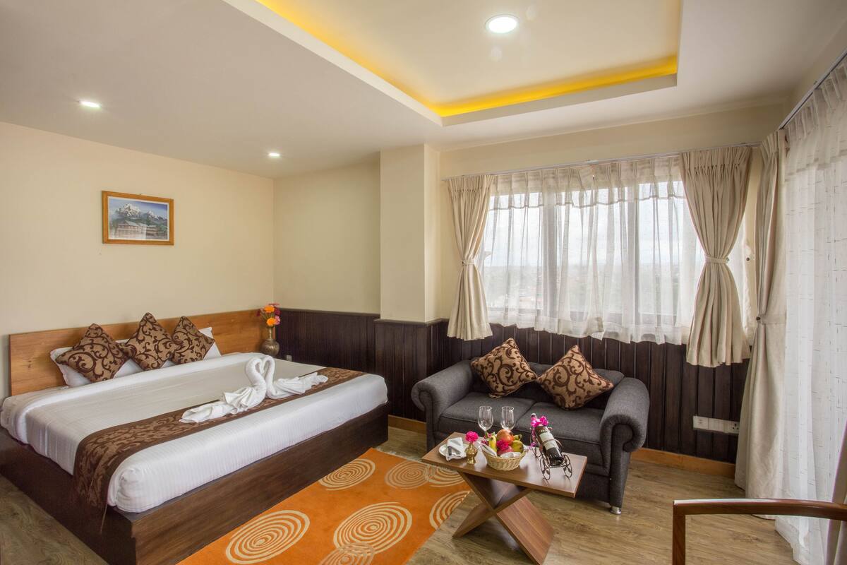 A hotel room with a double bed, a sofa, a small table with a tray of items, and a window with curtains.