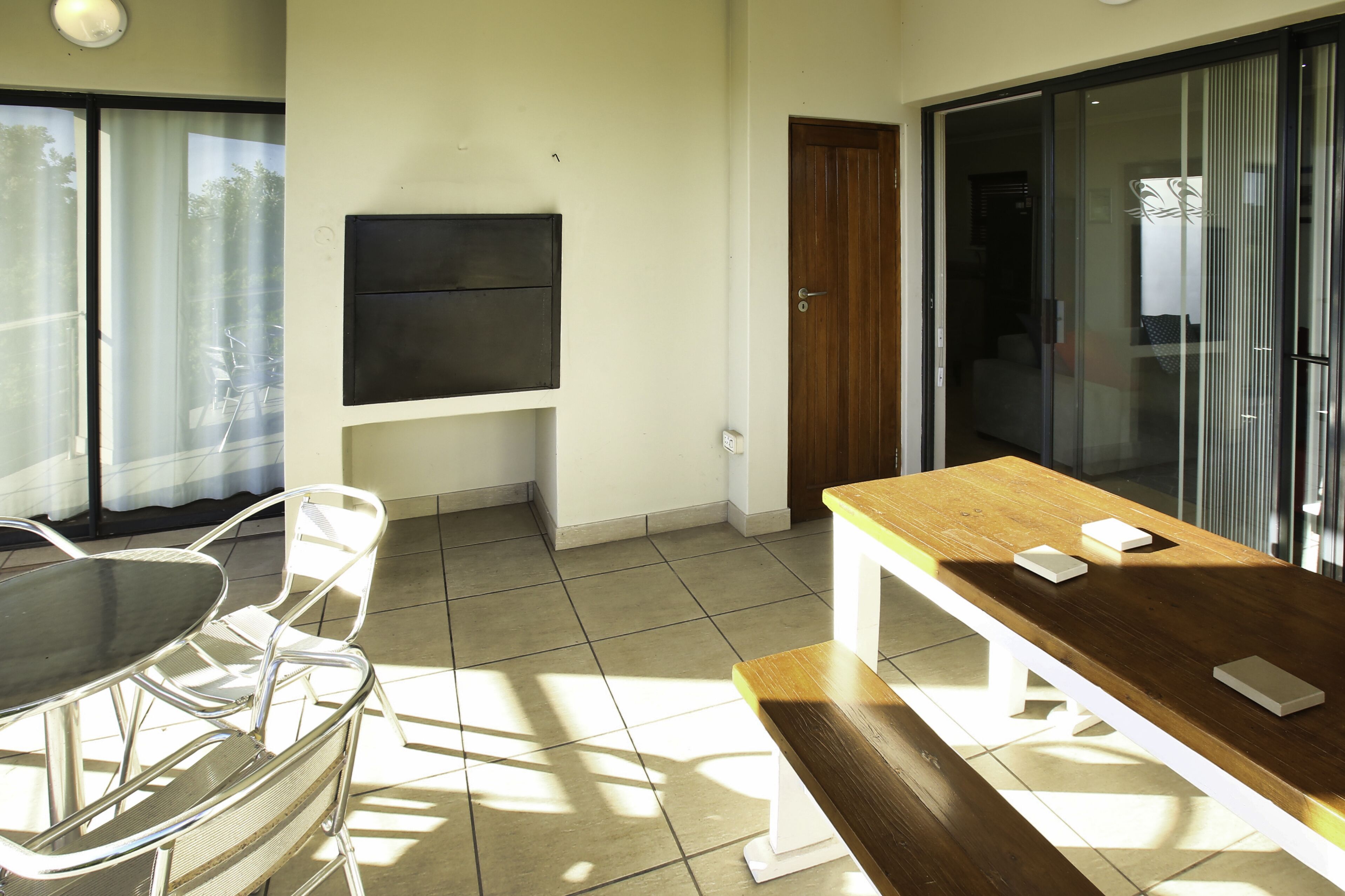Een kamer met een eettafel, stoelen, een aan de muur bevestigde televisie en een schuifdeur naar een buitenruimte.