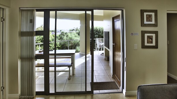 A room with a sliding glass door leading to a balcony with a table and chairs. - Ellefsen Golf Suite 137, Langebaan, 4 - Sleeper (Langebaan)