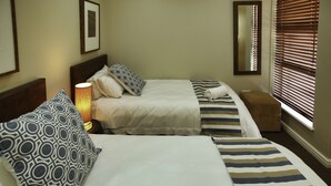 A hotel room with two beds, each with patterned pillows, a bedside lamp, and a small ottoman. - Ellefsen Golf Suite 137, Langebaan, 4 - Sleeper (Langebaan)