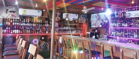 Un bar con sillas de madera, una barra y estantes llenos de botellas.