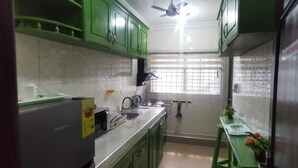 A kitchen with green cabinets, a stainless steel sink, and a window with bars.