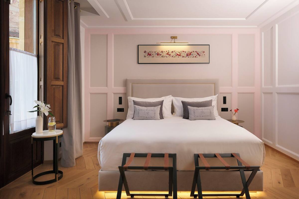 Een netjes ingerichte slaapkamer met een groot bed, nachtkastjes en een klein tafeltje met een vaas en bloemen.