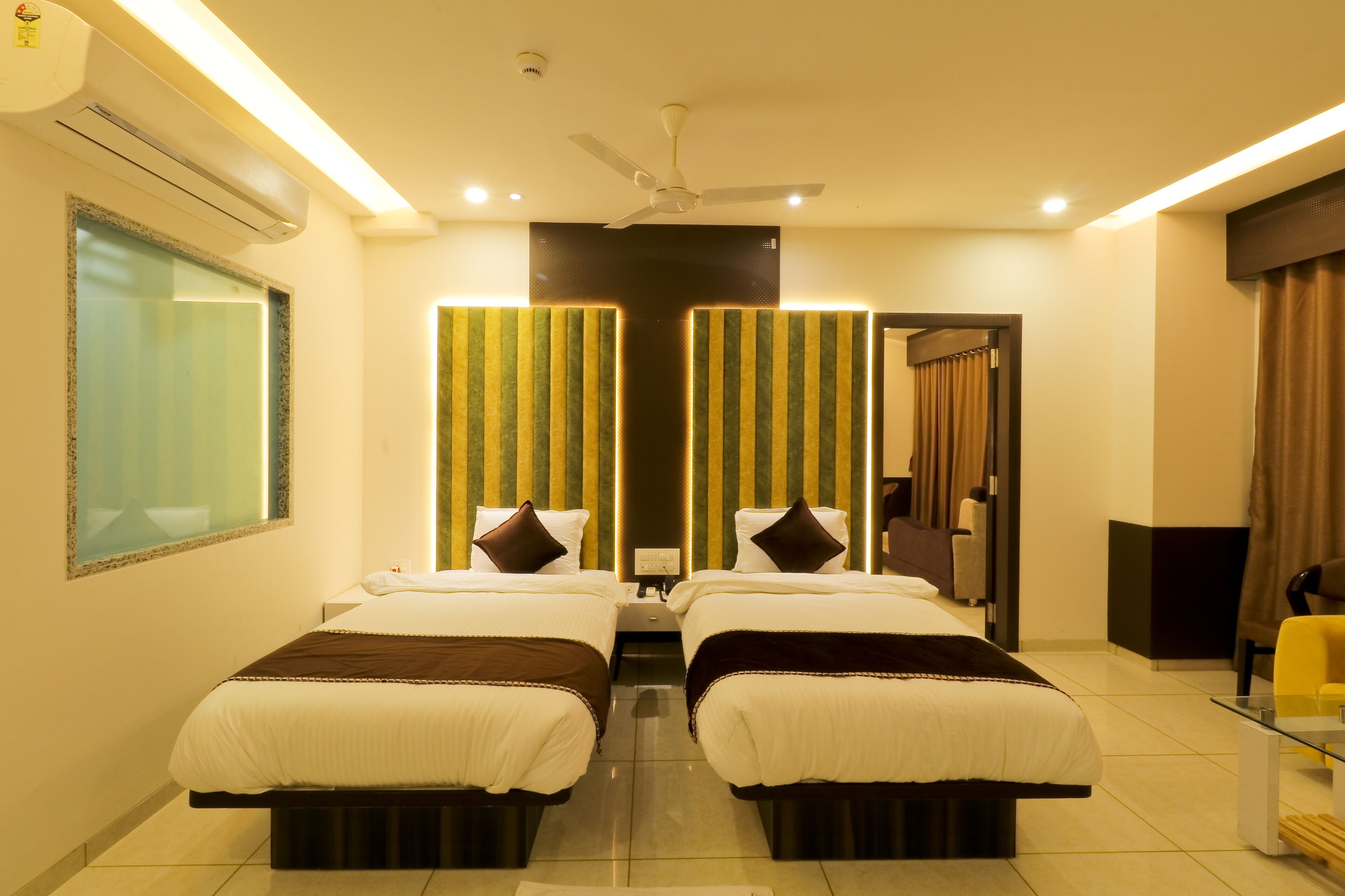 A hotel room with two beds, a ceiling fan, a TV, and a glass table.