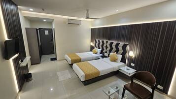 A modern hotel room with two beds, a glass coffee table, a brown chair, a TV, and a ceiling fan.