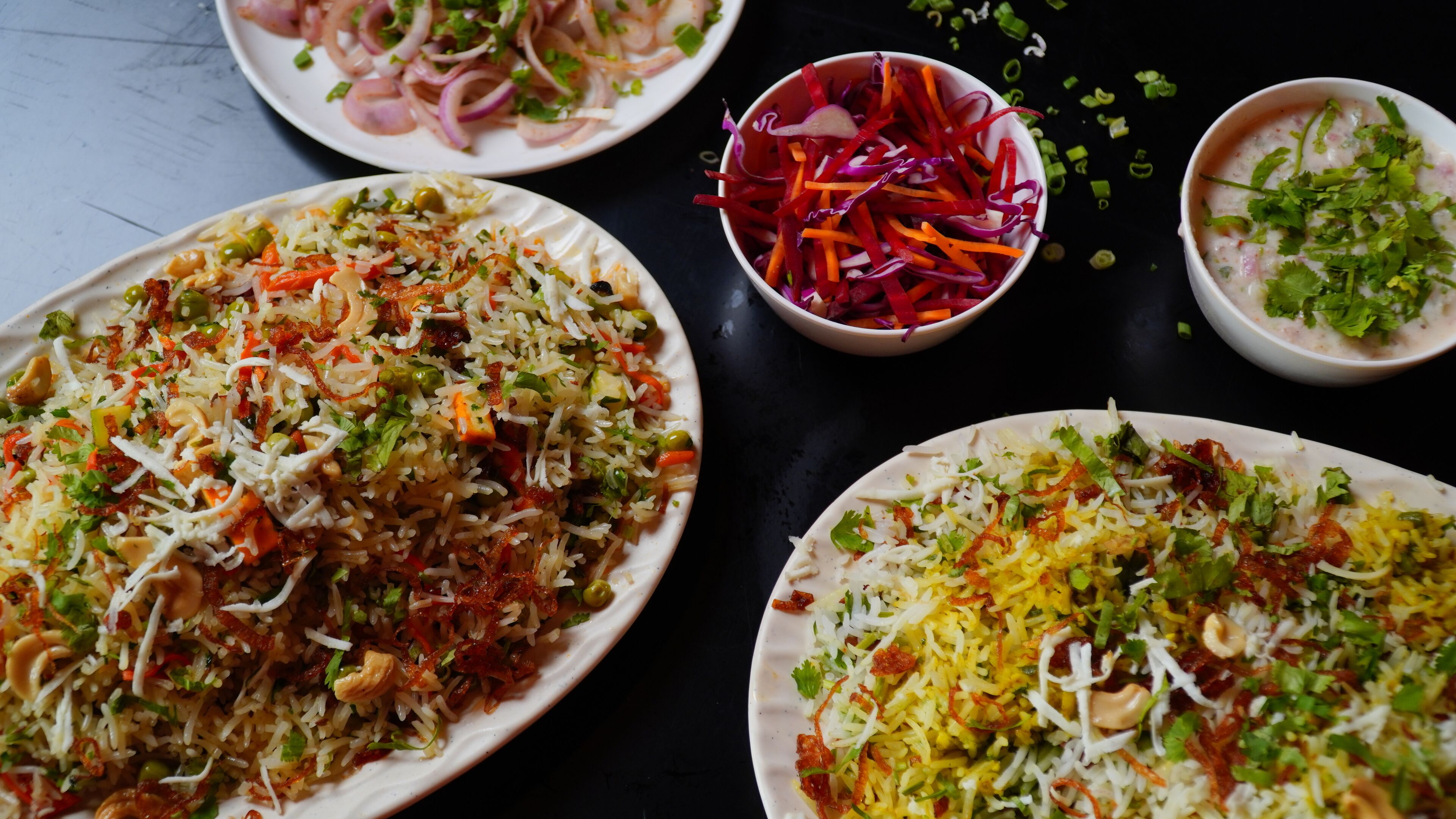 A variety of dishes including biryani, a vegetable salad, and a creamy dish, likely served on a table.