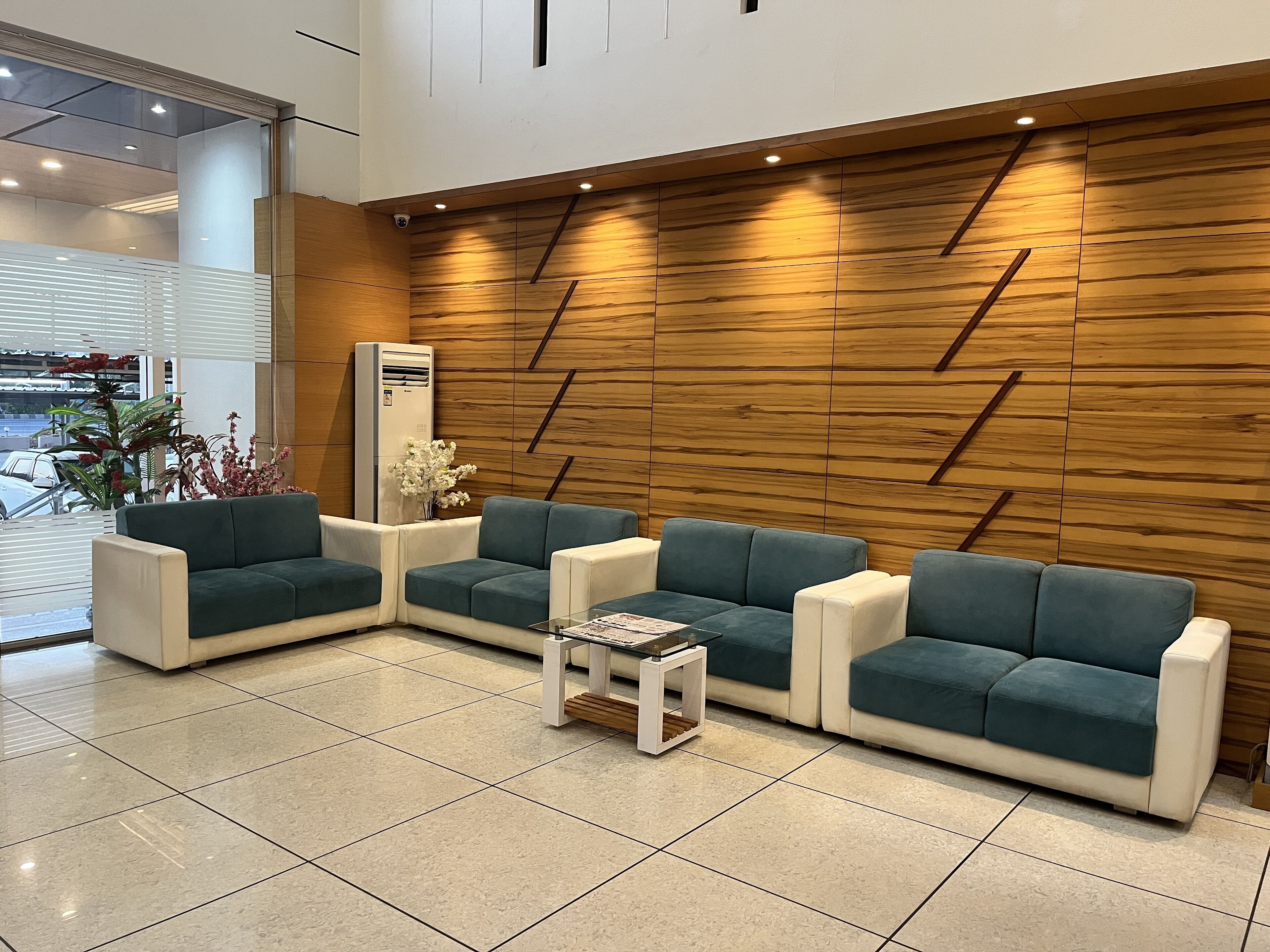 A modern lobby with a wooden accent wall, two sofas, a coffee table, and a potted plant.
