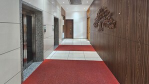 Un pasillo moderno con ascensores, alfombra roja y una pared de madera con diseño de hojas.