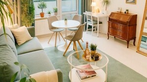 Ein modernes Wohnzimmer mit einem grünen Sofa, einem runden Couchtisch und einem Essbereich mit weißem Tisch und Stühlen.