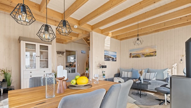 A modern living room with a wooden dining table, grey sofa, and a kitchen in the background. - Skippers Home - Terrace, Fireplace, Infrared Sauna, Free Pets Allowed (Olpenitz)