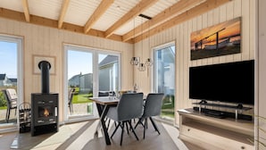 A modern living room with a fireplace, dining area, and TV. - Skippers Home - Terrace, Fireplace, Infrared Sauna, Free Pets Allowed (Olpenitz)