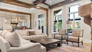 A spacious living room with a sectional sofa, a coffee table, and a fireplace. There is a large window providing natural light and a view of the outdoors. - Spacious Home in Appalachian Mountains - Hot Tub, Firepit, on the Tocccoa River! (Suches)