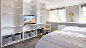 Quarto de hotel com cama, televisão em uma estante, janela com vista e cestos organizadores.