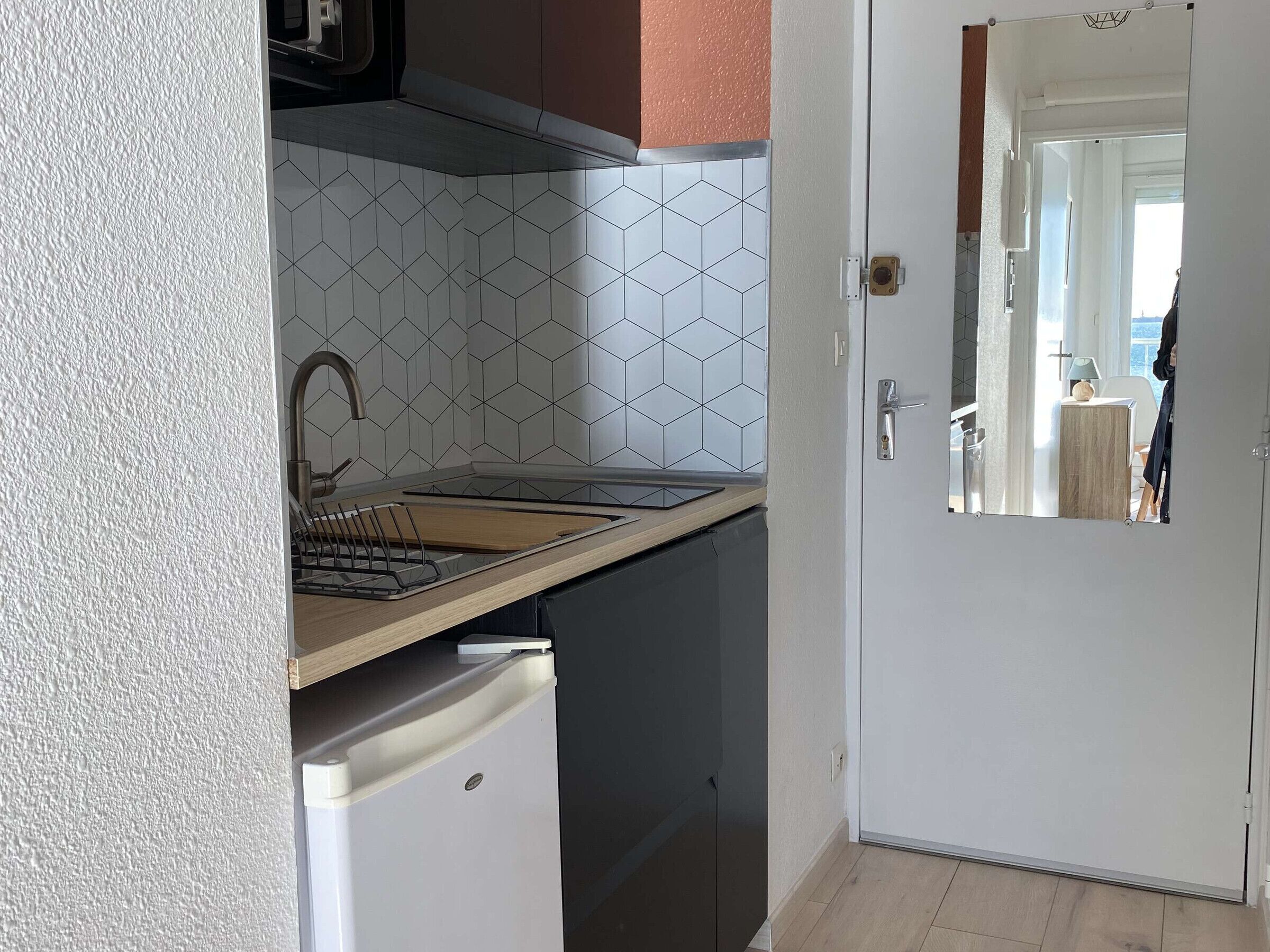 Une cuisine compacte au design moderne, comprenant un évier, un petit réfrigérateur et un crédence carrelée.