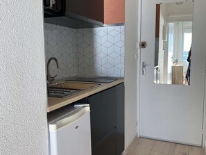 A compact kitchen with a modern design, featuring a sink, a small refrigerator, and a tiled backsplash. - Air-conditioned studio with WIFI, Thau Lagoon view (Balaruc-les-Bains)