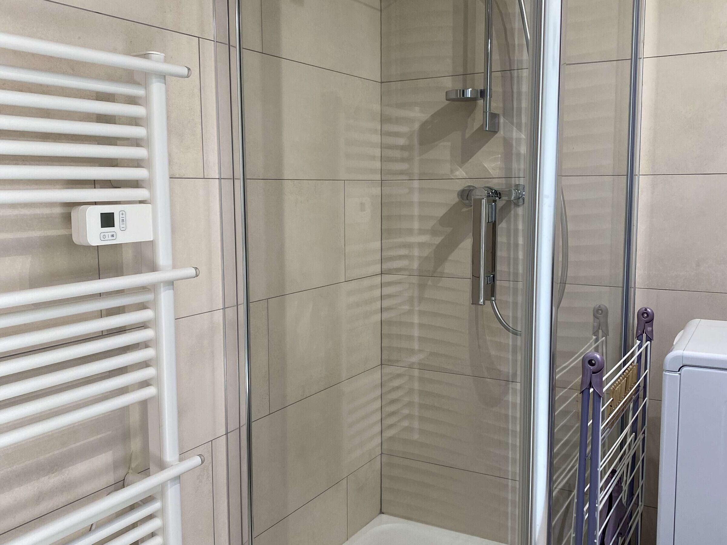 Un espace douche doté d’une porte en verre, d’un porte-serviettes blanc et d’un panneau de commande.