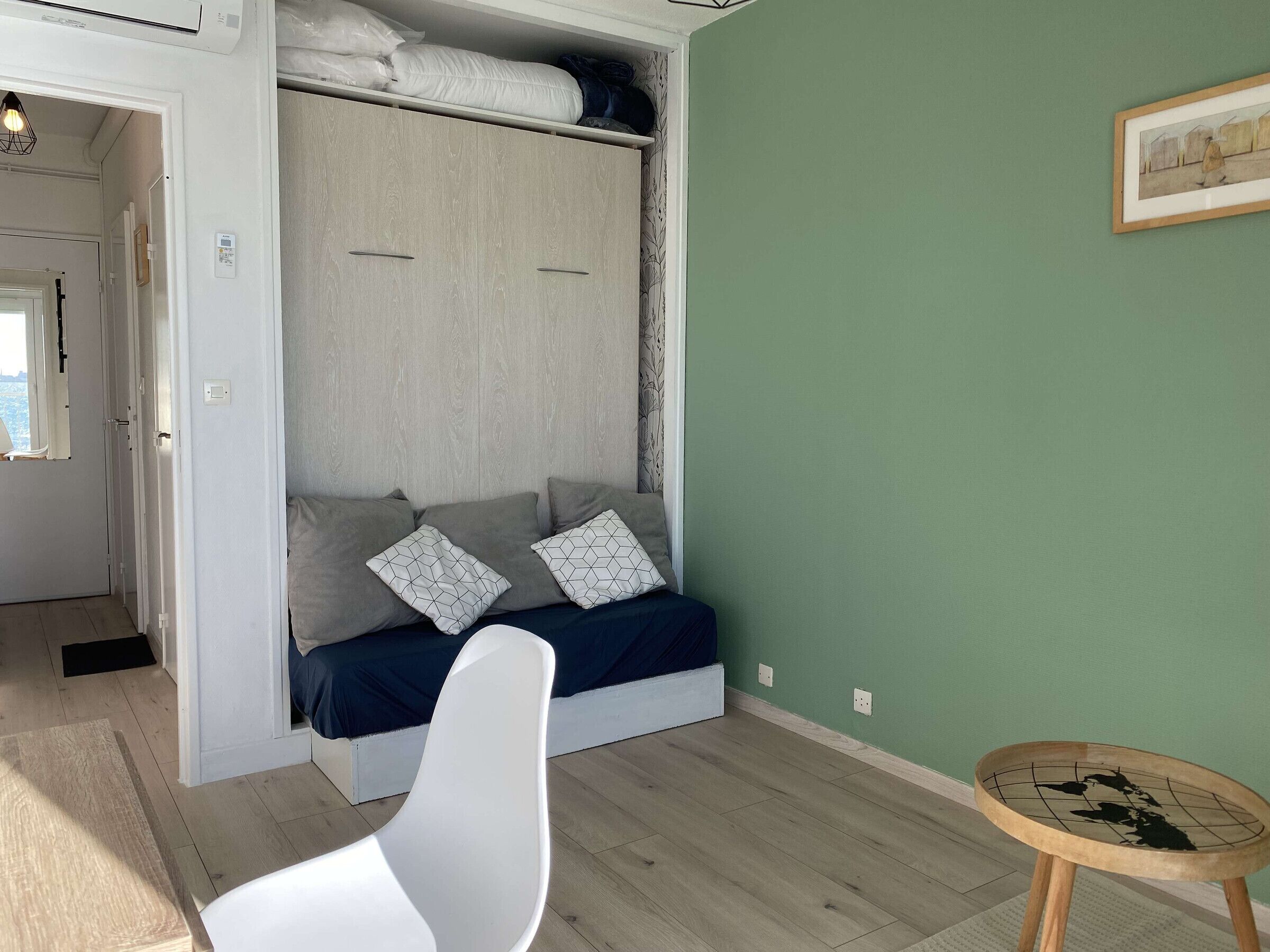 Une pièce avec un lit, une chaise blanche, une petite table et un mur vert.