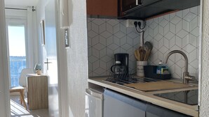 A modern kitchen with a built-in stove, a coffee maker, and a sink. There is a window with a view of the sea. - Air-conditioned studio with WIFI, Thau Lagoon view (Balaruc-les-Bains)