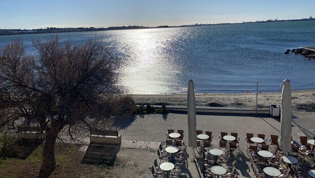 A waterfront restaurant with outdoor seating overlooking a body of water, a tree in the foreground, and a clear sky. - Air-conditioned studio with WIFI, Thau Lagoon view (Balaruc-les-Bains)