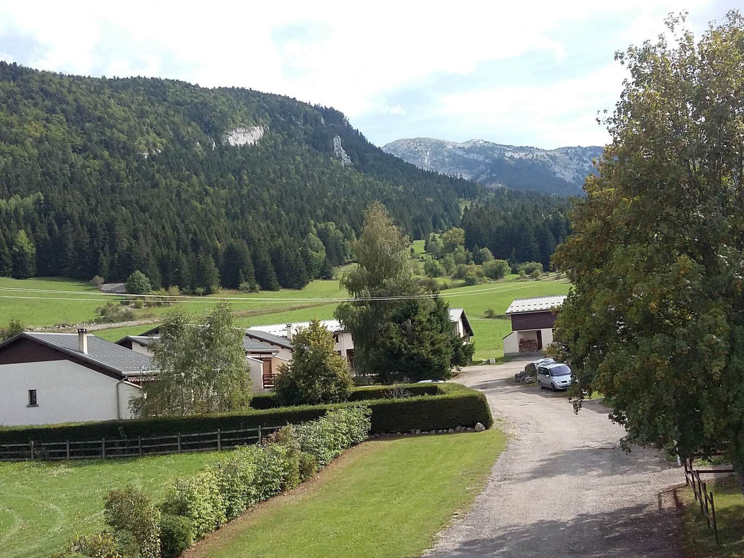 Entorno rural con casas, un camino de grava y montañas al fondo.