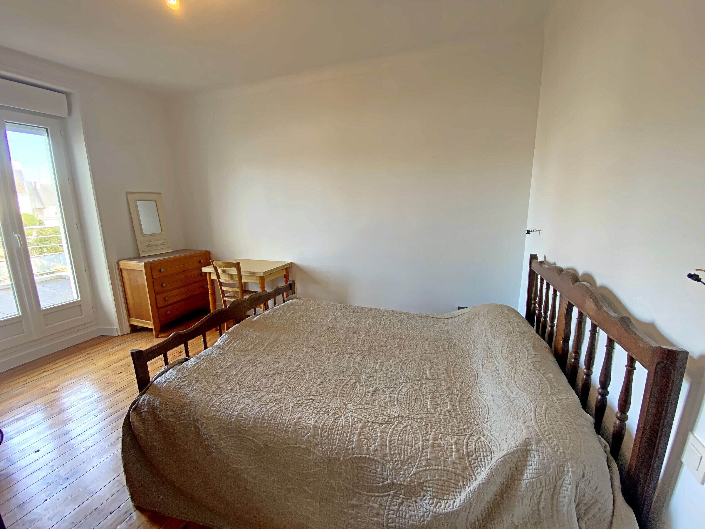 Un dormitorio con una cama de madera, un aparador de madera, una silla y una mesita.