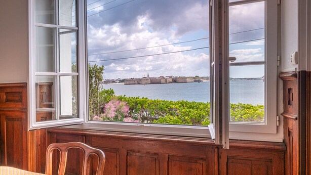 Ein Zimmer mit großem Fenster mit Blick auf ein Gewässer und eine entfernte Insel.