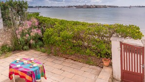 Eine Terrasse mit Esstisch, einem Tor und Blick auf das Meer sowie eine entfernte Festung.