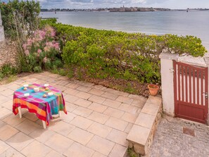 En terrasse med spiseplads, en port og udsigt til havet samt en fjerntliggende fæstning.