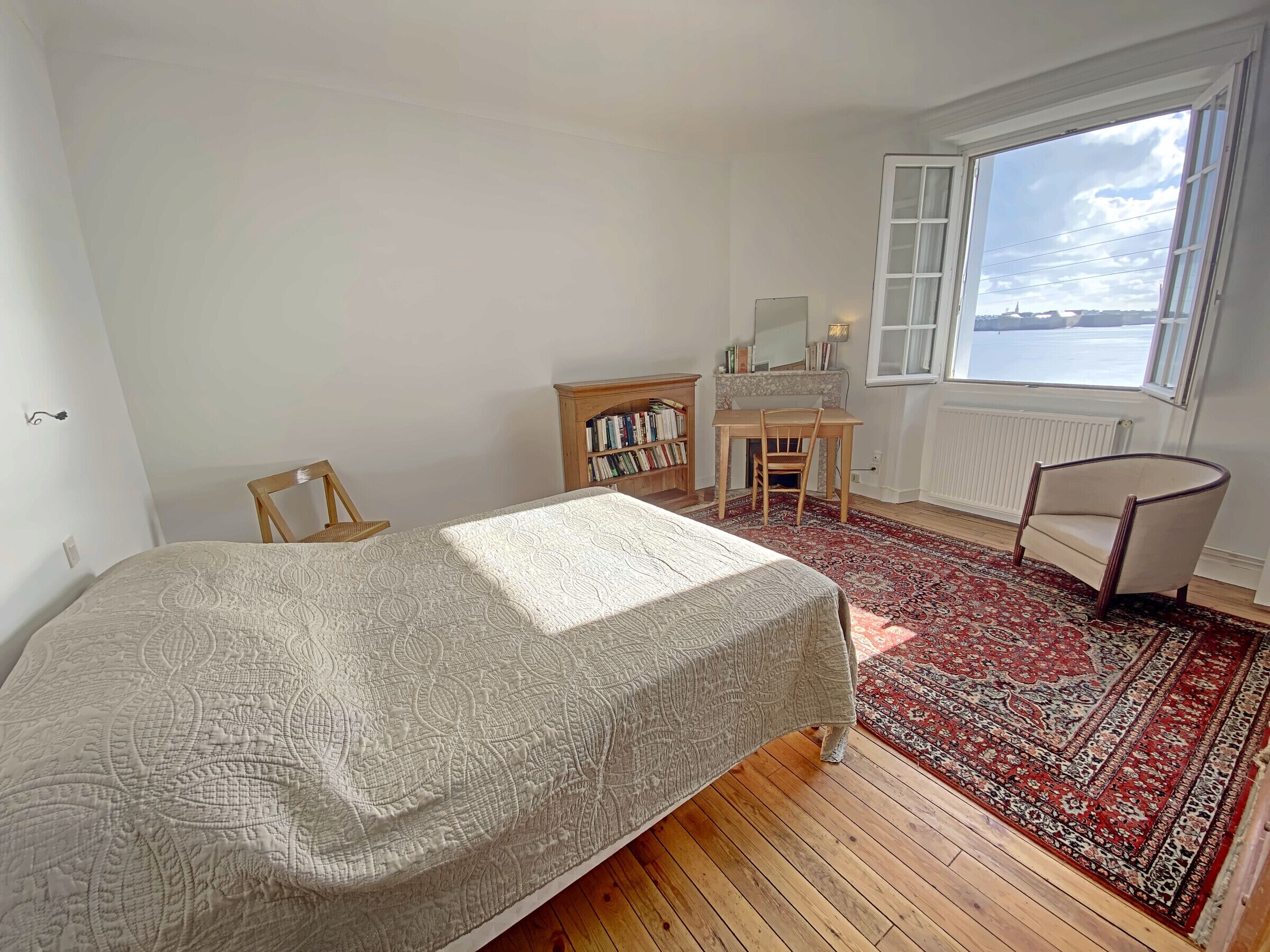 A bedroom with a bed, a desk, a chair, a bookshelf, and a view of the outside.