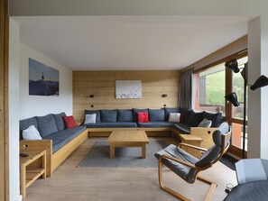 Una sala de estar moderna con piso de madera, un sofá modular, una mesa de centro de madera y un sillón mecedor.