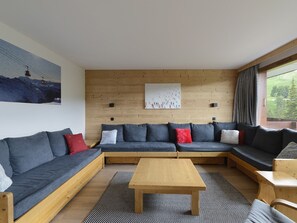 A modern living room with a wooden floor, a central coffee table, and a sectional sofa with multiple cushions.