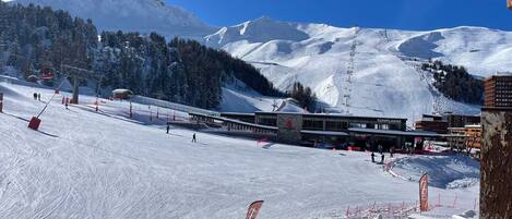 A ski resort with a ski lift, buildings, and snow-covered mountains.