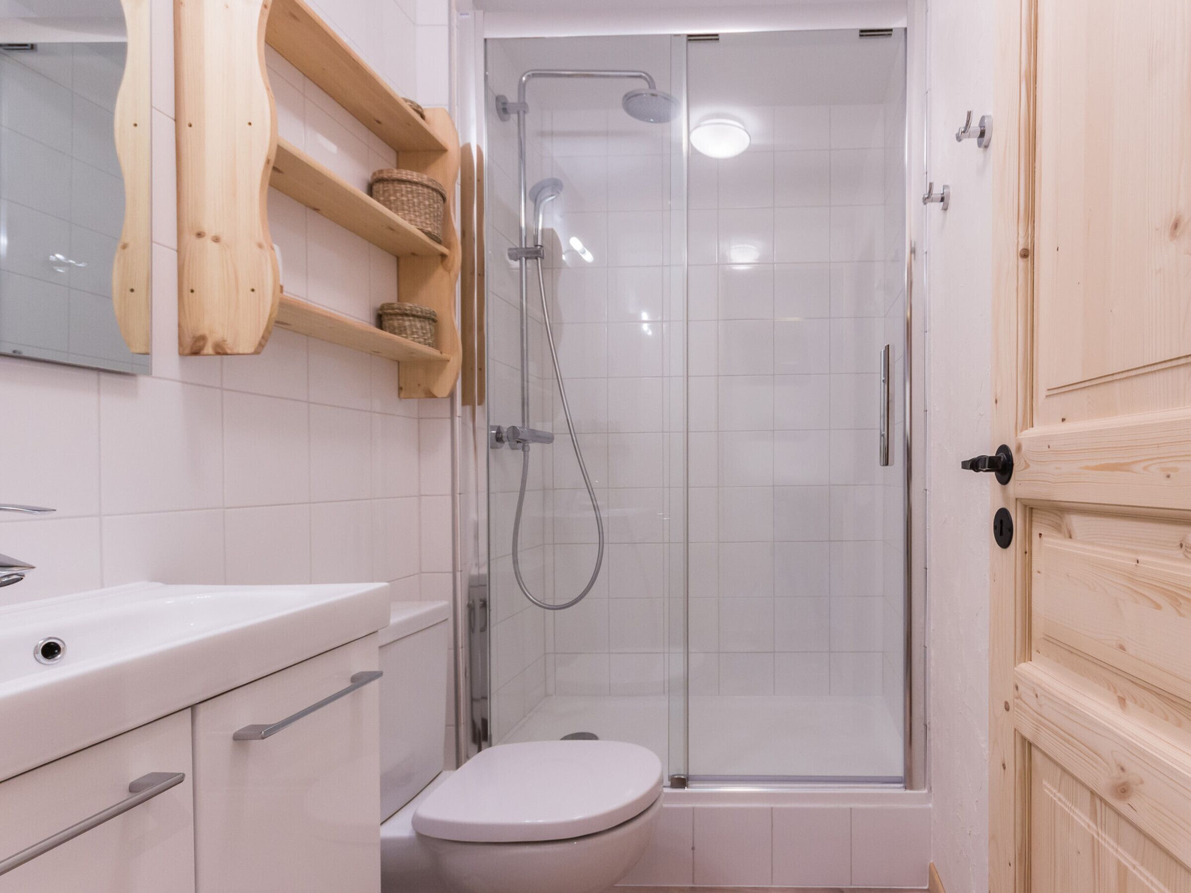 Un baño con inodoro, cabina de ducha y estanterías de madera.