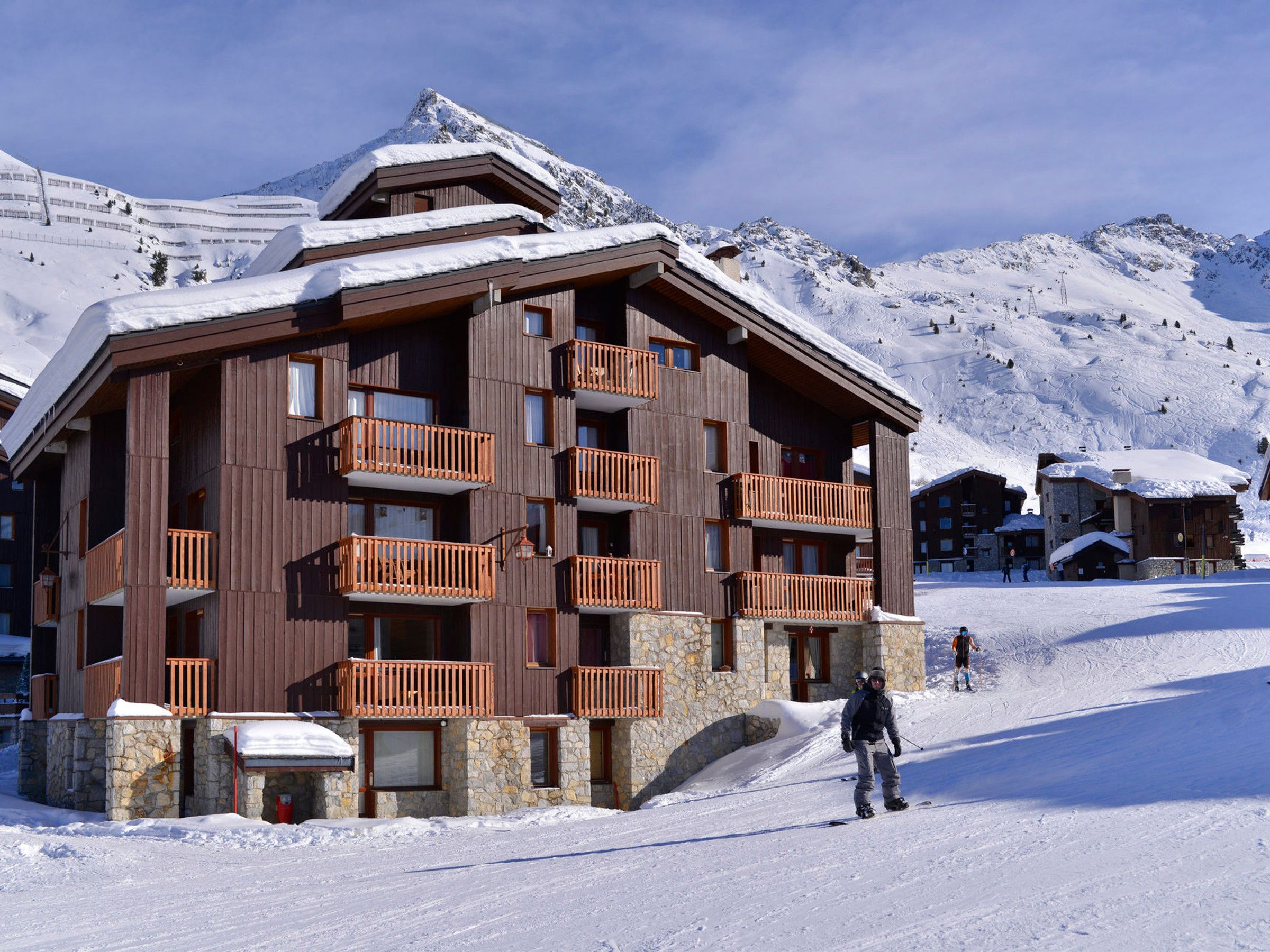 A multi-story wooden building with balconies, set against a snowy mountain backdrop.