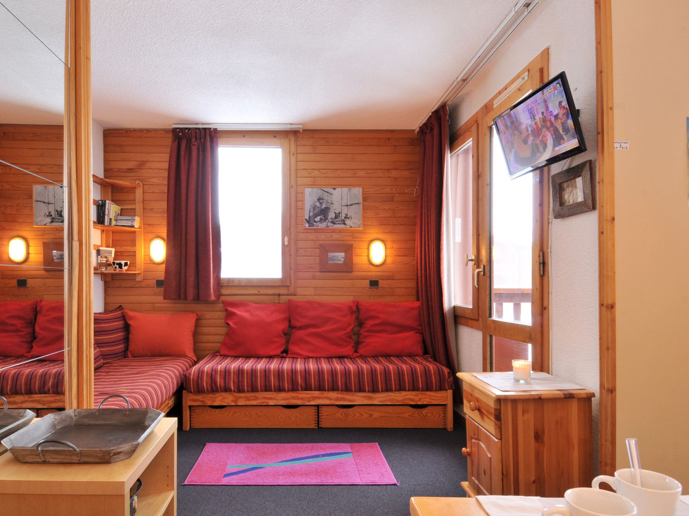 A cozy cabin-style room with two wooden beds, a television, and a small table with a candle.