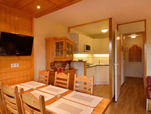 Uma sala de jantar com uma mesa de madeira, cadeiras e uma televisão na parede.