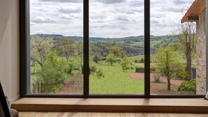 Une pièce dotée d’une grande fenêtre donnant sur un paysage verdoyant et un bâtiment en pierre.