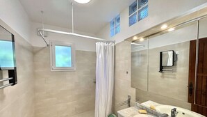 A modern bathroom with a shower, a window, a large mirror, and two sinks.